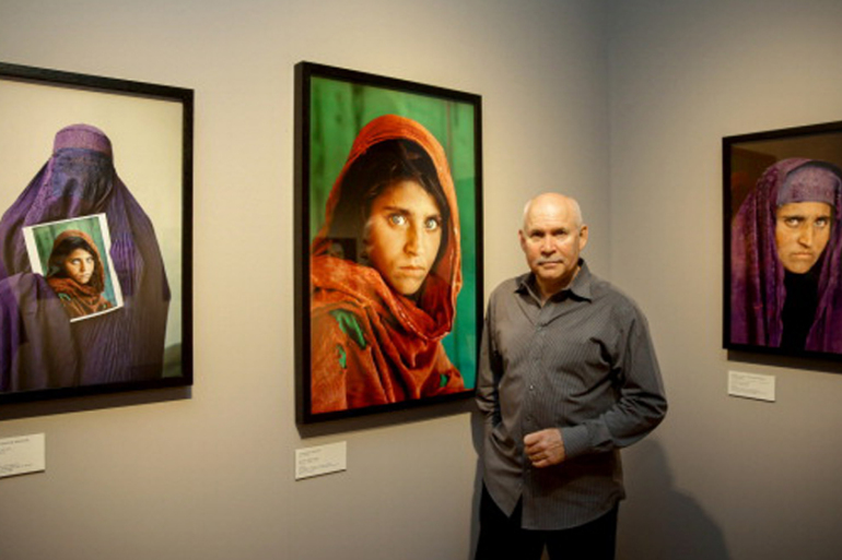 US photographer Steve McCurry poses next to his photos of the "Afghan Girl" named Sharbat Gula at the opening of the "Overwhelmed by Life" exhibition of his work at the Museum for Art and Trade in Hamburg, northern Germany on June 27, 2013. The exhibition comprises some 120 photographs taken between 1980 and 2012 in countries such as Afghanistan, the United States, Pakistan, India, Tibet, Kashmir, Cambodia, Indonesia, Burma and Kuwait.  AFP PHOTO / DPA / ULRICH PERREY   GERMANY OUT RESTRICTED TO EDITORIAL USE, MANDATORY MENTION OF THE ARTIST UPON PUBLICATION, TO ILLUSTRATE THE EVENT AS SPECIFIED IN THE CAPTION        (Photo credit should read ULRICH PERREY/AFP/Getty Images)